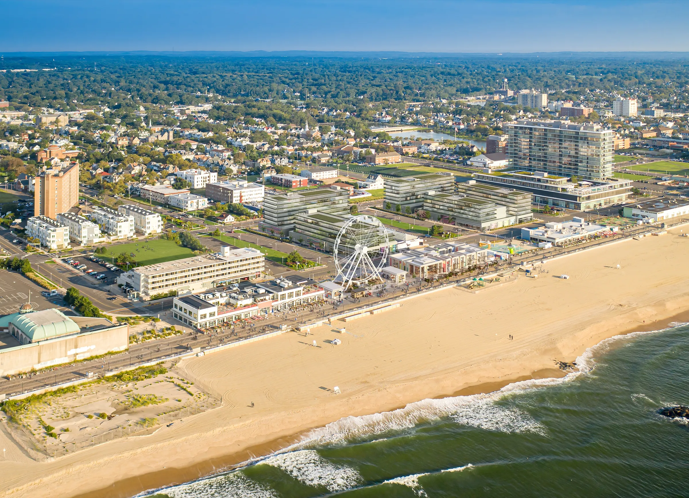 High aerial 3D rendering of the Asbury Park beachfront, the pavilion development and Ferris wheel set along the boardwalk between the town grid and the wide beach and ocean.