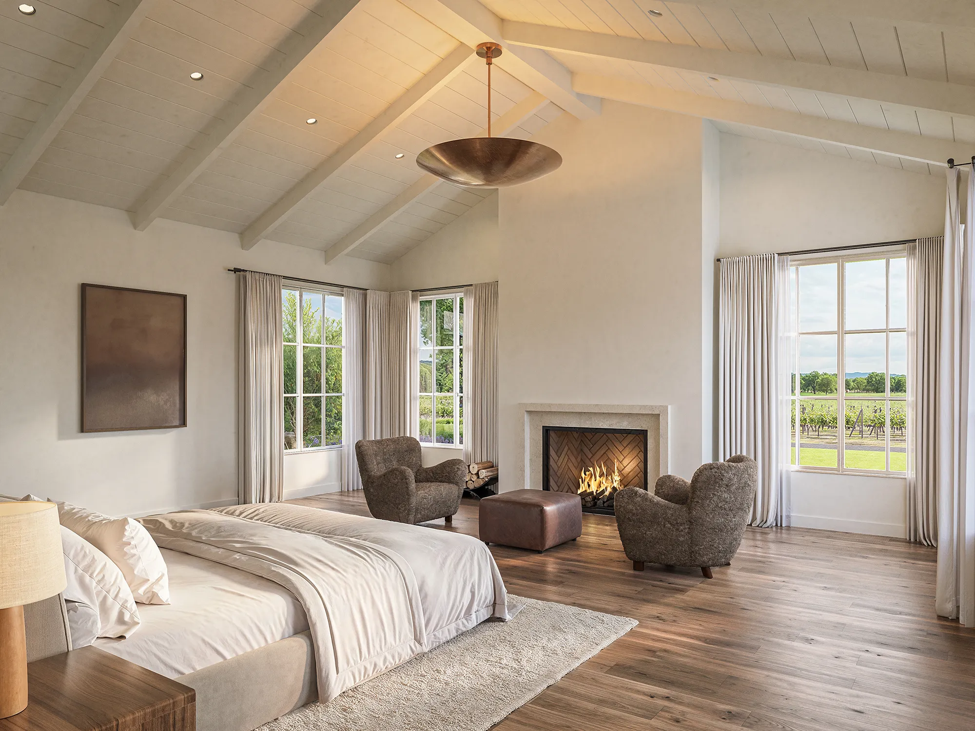 Interior 3D rendering of the primary suite at a Napa Valley estate in St. Helena, a bed under exposed ceiling beams, a stone fireplace between two shearling chairs, and tall windows looking out to the vineyards.