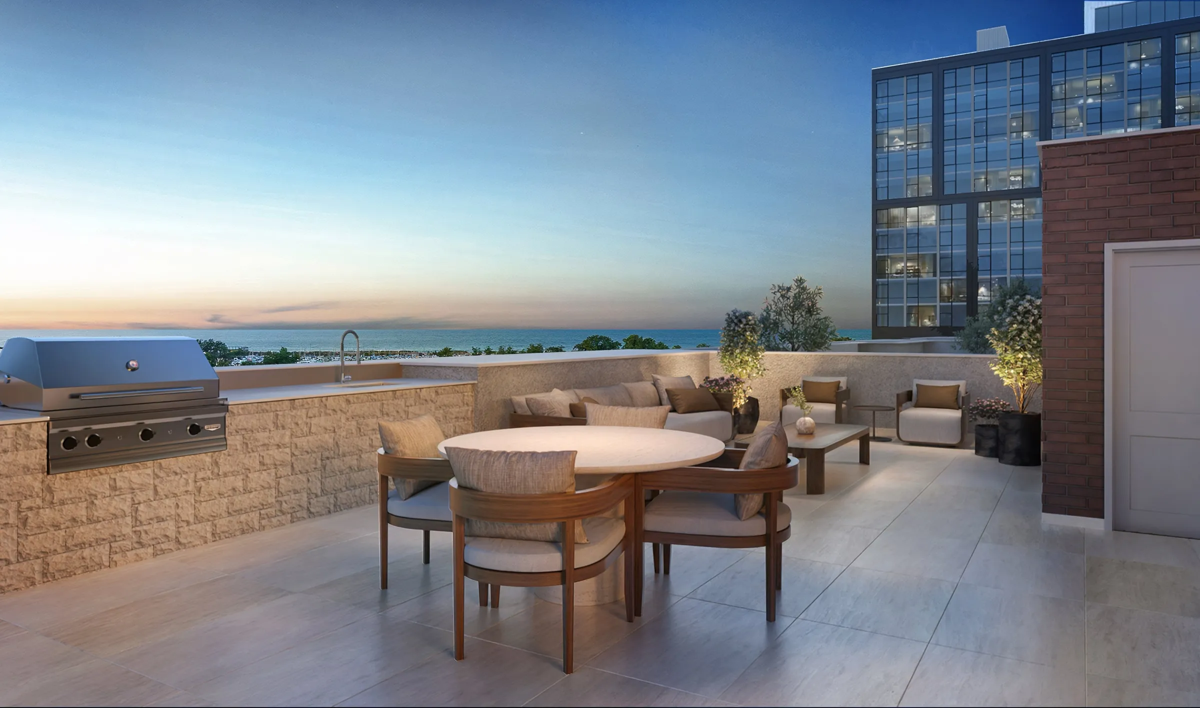 Twilight 3D rendering of a townhome rooftop deck at SoLa in Michigan City, Indiana, with a built-in grill and outdoor kitchen, a round dining table, a lounge sofa, and a view over Lake Michigan beside a neighboring tower.